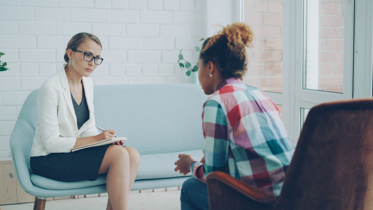 A therapist listens and takes notes while a client speaks during a counseling session.