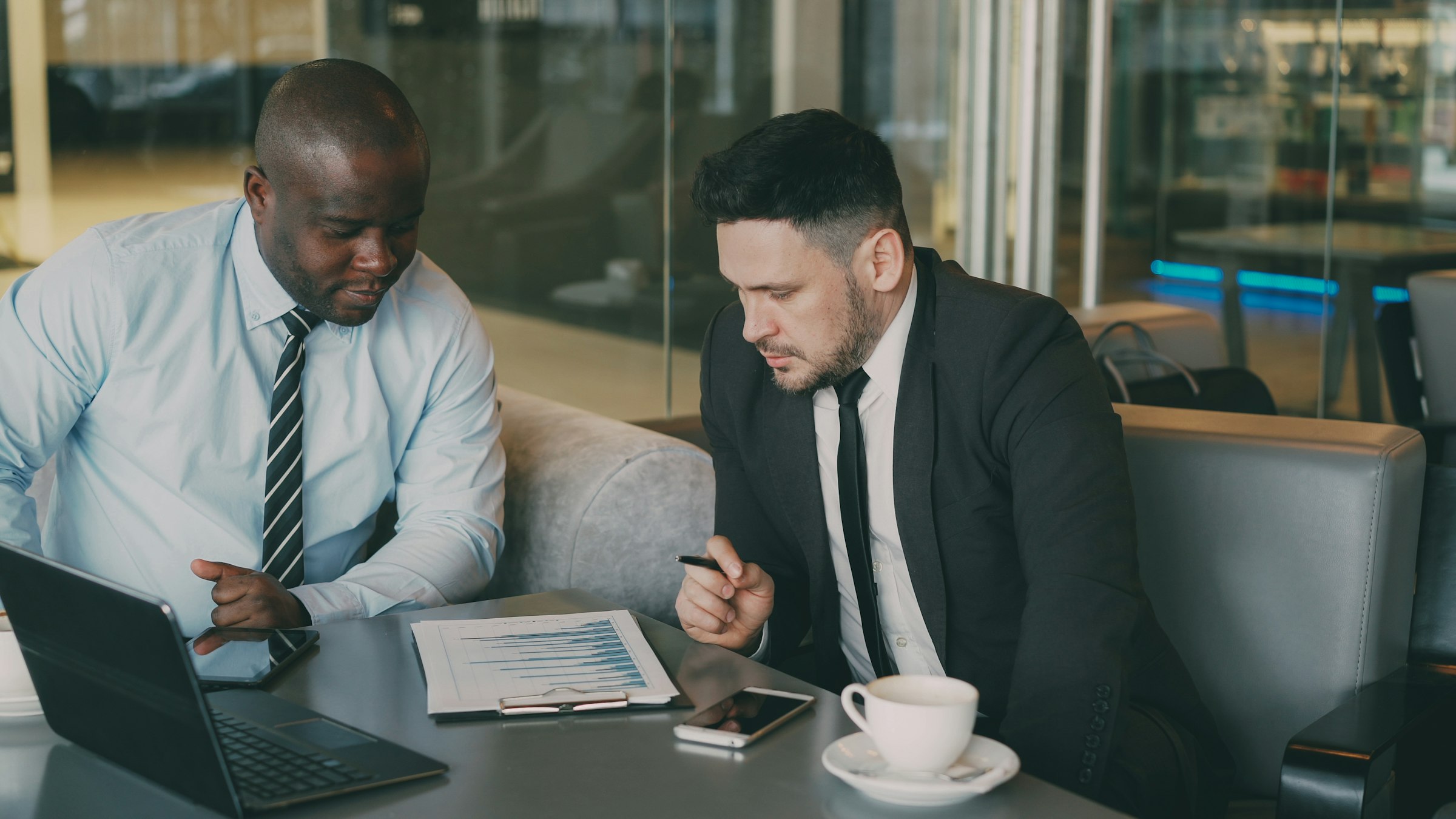 Two colleagues in business attire review certification documents together at a table.
