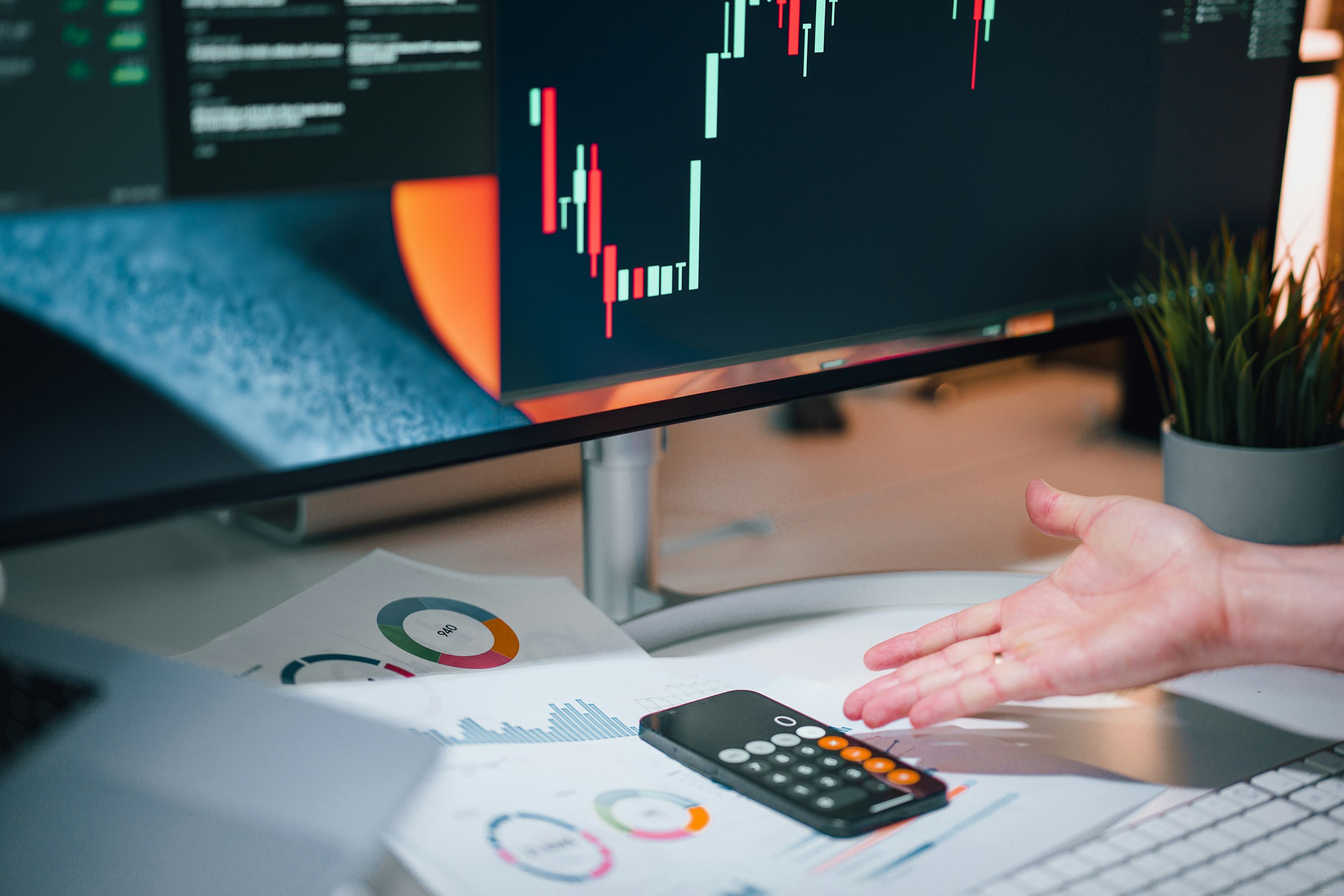A hand pointing at a calculator beside financial documents on an office desk.