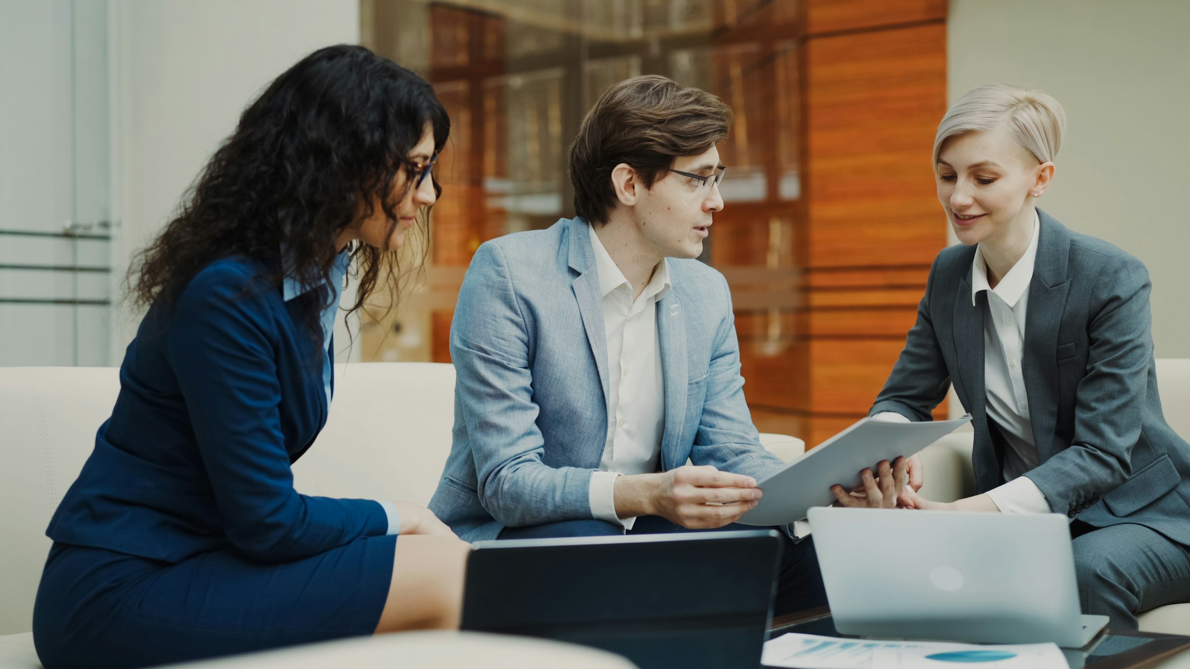 Three colleagues discuss standards documentation together at a table in an office setting.